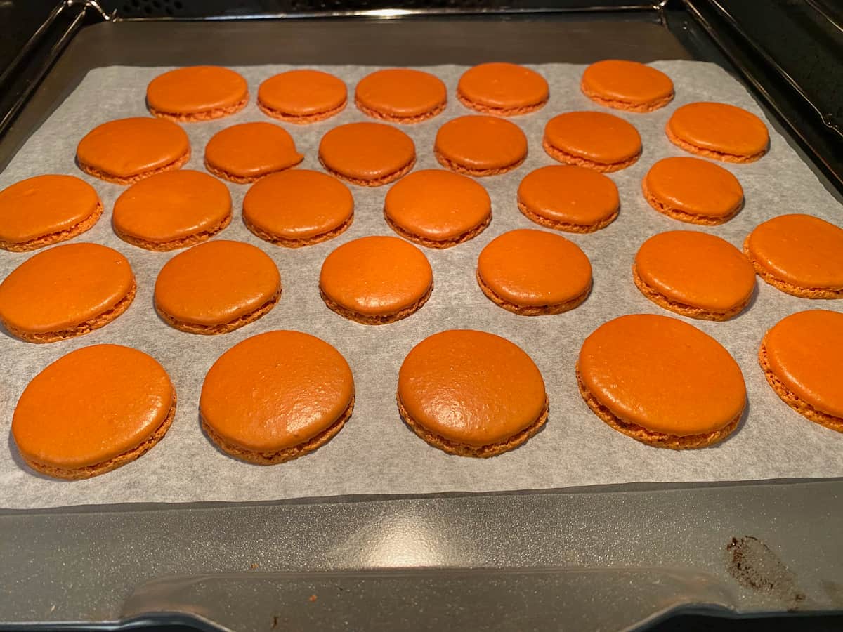 shiny macaron shells on a baking tray in the oven