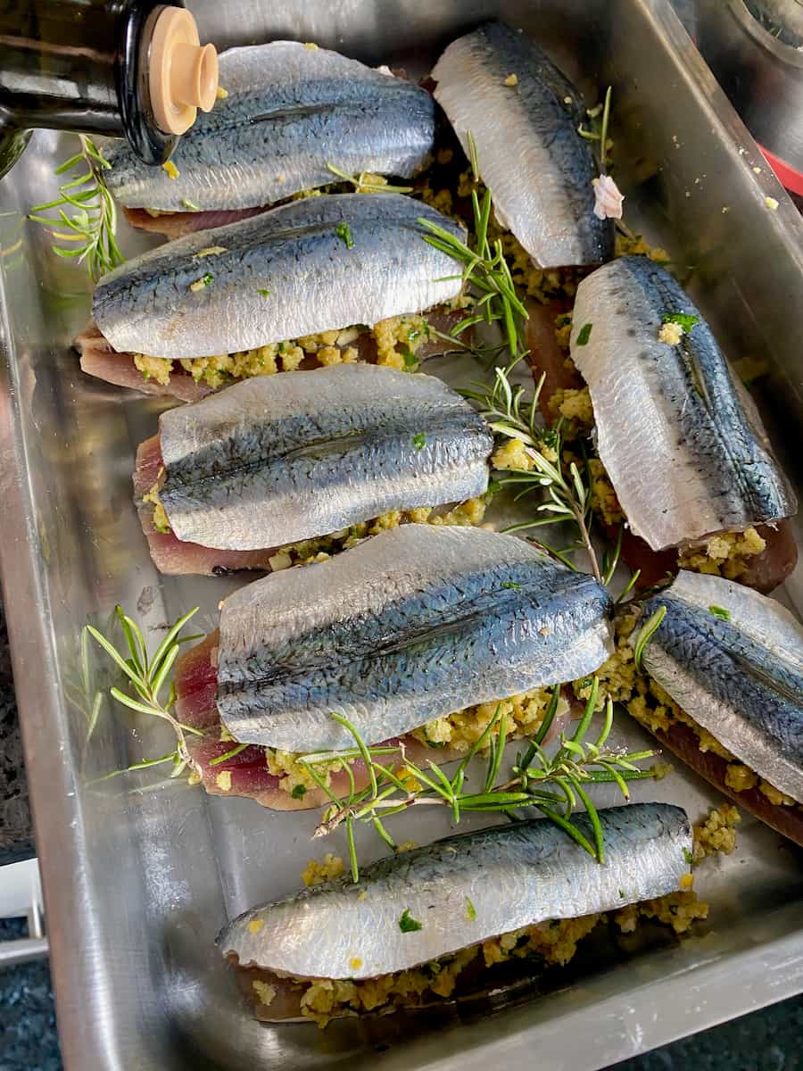 pouring olive oil over filleted sardines stuffed with herbs and breadcrumbs in a roasting tin