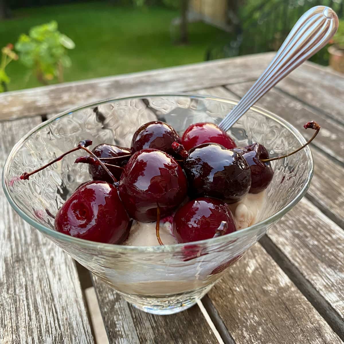glass dish of ice cream topped with glistening roasted cherries