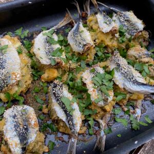 two rows of whole sardine fish stuffed together in a roasting dish with fresh parsley