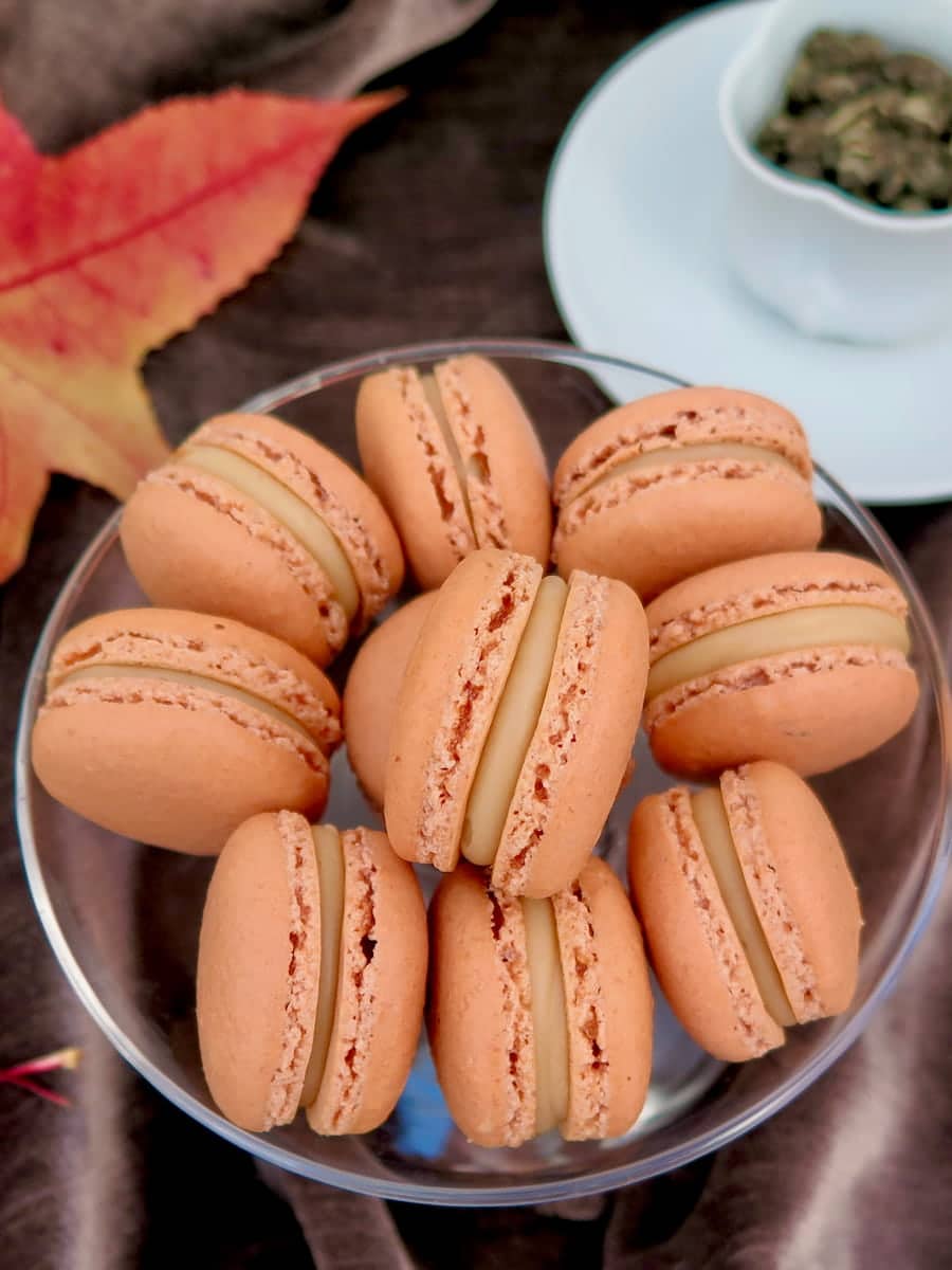 bowl of light caramel French macarons with a thick filling between perfect ruffled feet