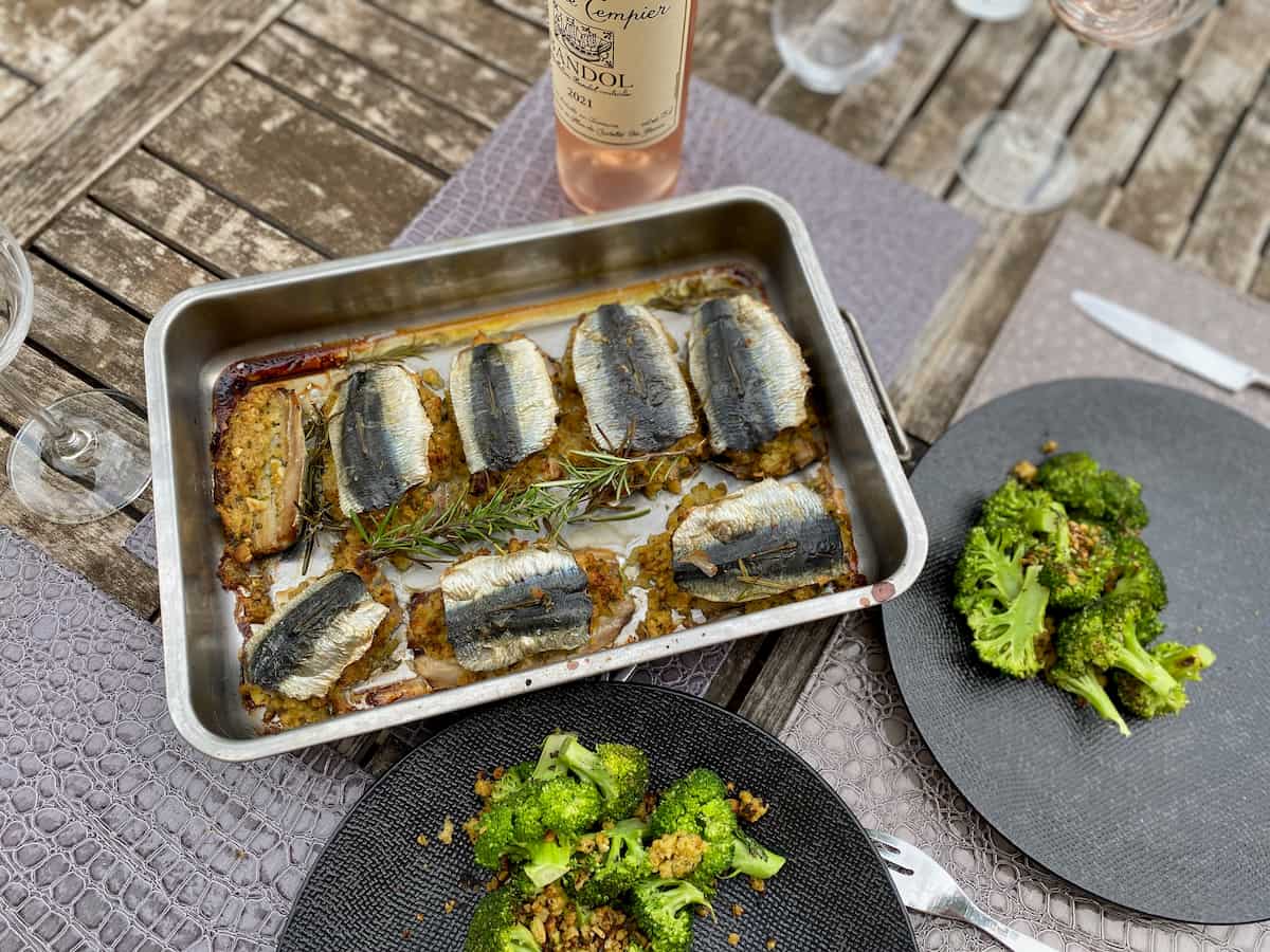 roasting tin with baked sardines stuffed with herbs, bottle of rosé wine and plates dressed with broccoli