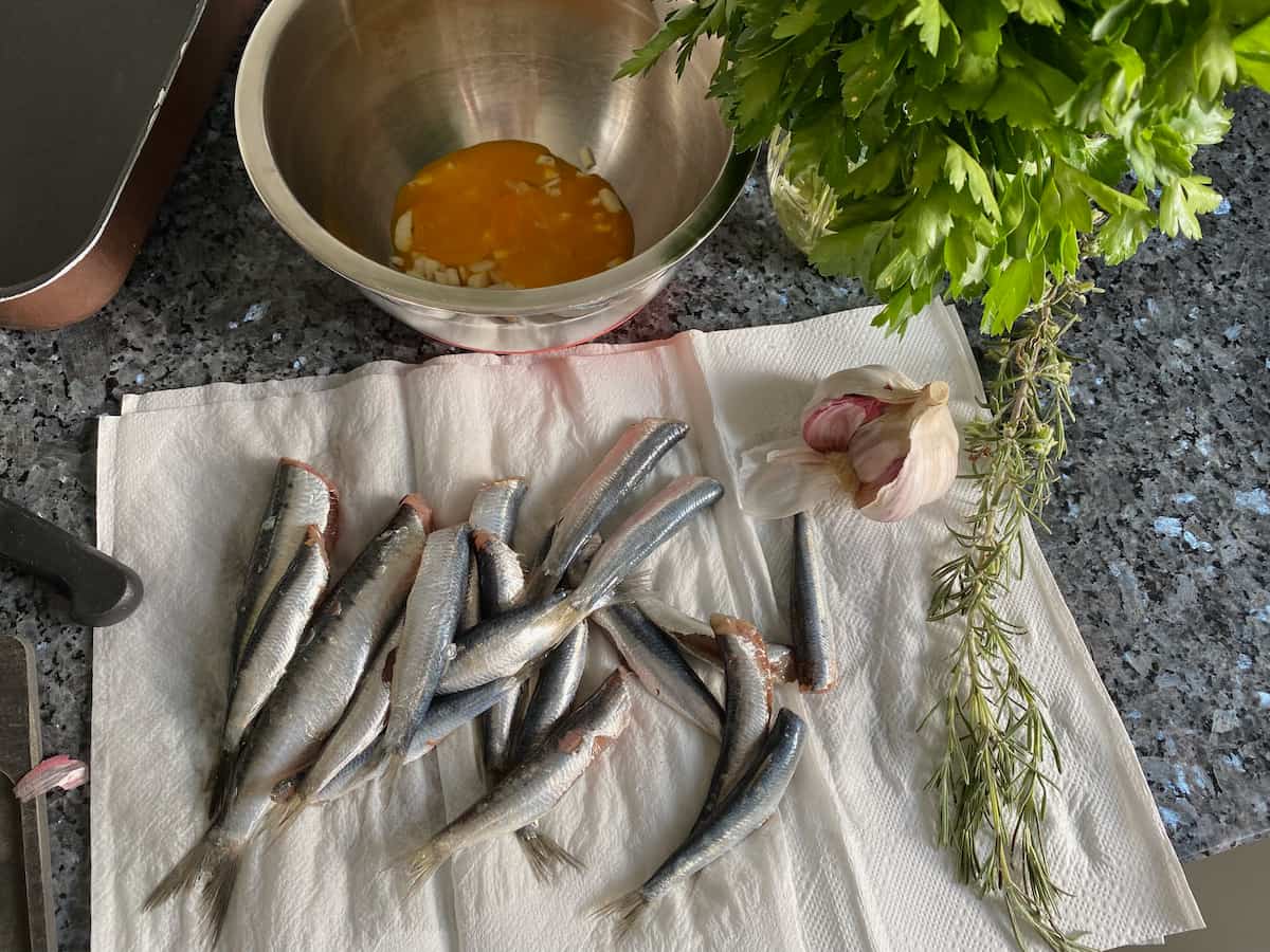 drying prepared sardines with tails on kitchen paper next to herbs, garlic and egg yolks