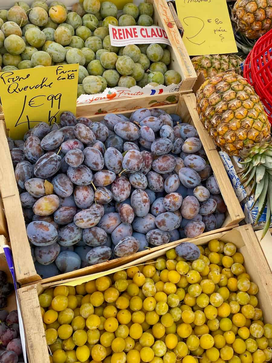 crates of French plums at the market, with signs saying Reine Claude, Quetche and a box of small yellow mirabelles