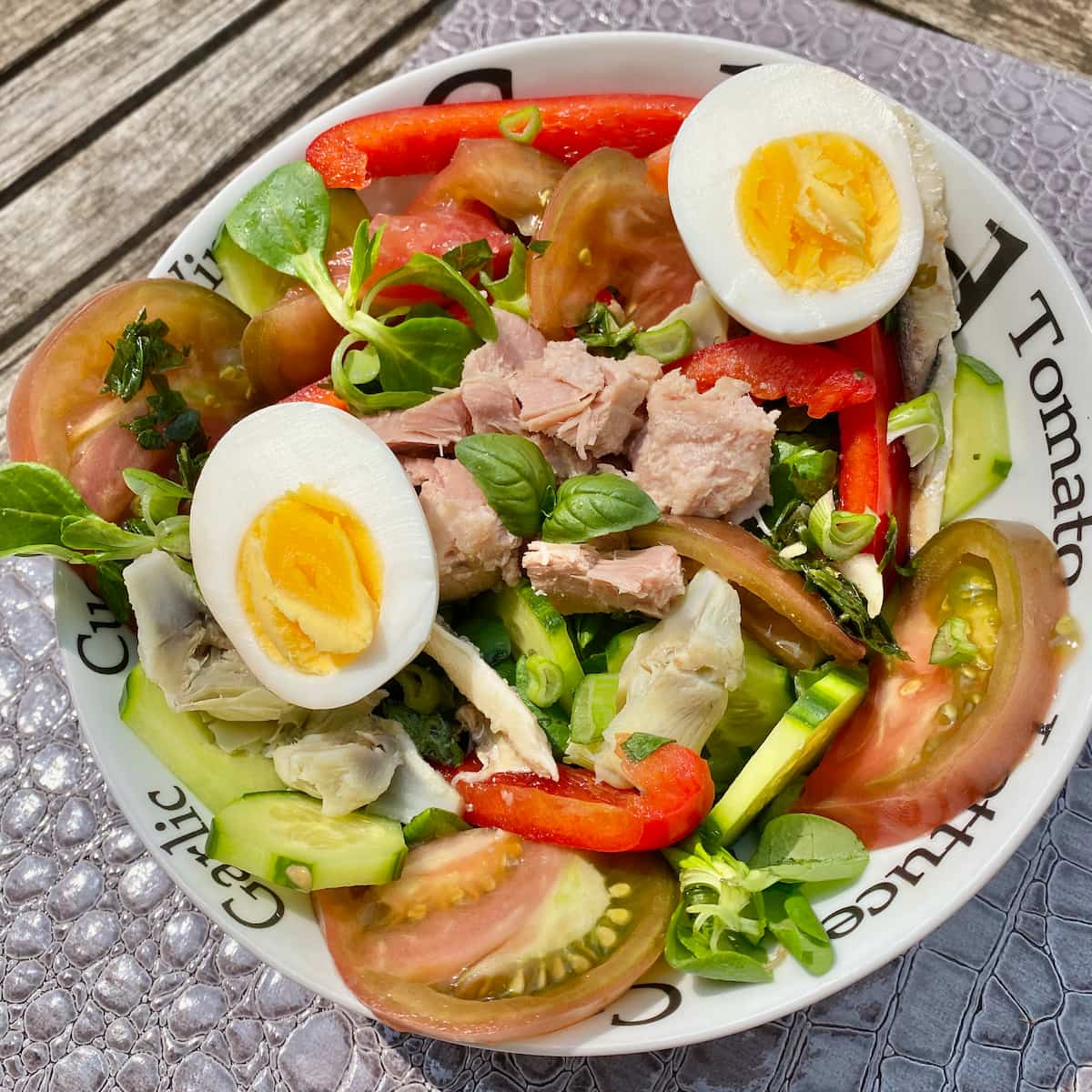 bowl of salad with boiled eggs, tomatoes, tuna, basil, cucumber, anchovies, peppers, salad leaves, spring onions, garlic and artichoke hearts