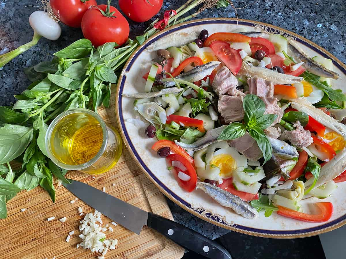 chopping up garlic finely with olive oil and basil next to the large plate of salad 