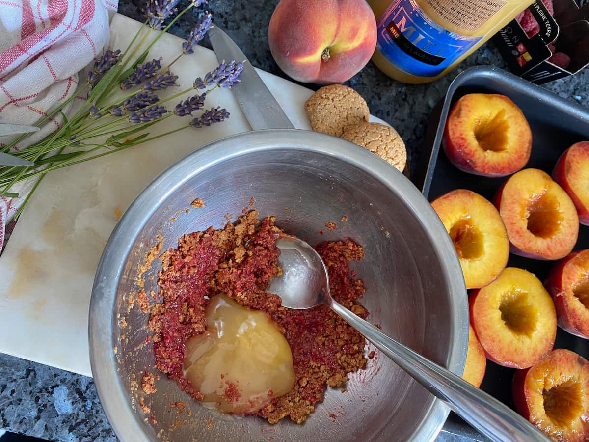 mixing crushed amaretti almond biscuits, raspberries and honey in a bowl next to a platter of halved peaches 