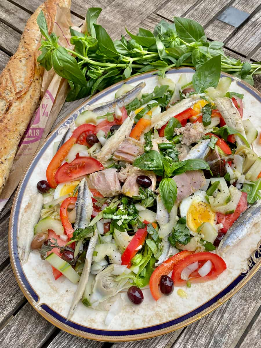 large plate with a raw salad of tuna, olives, tomatoes, basil and other fresh vegetables