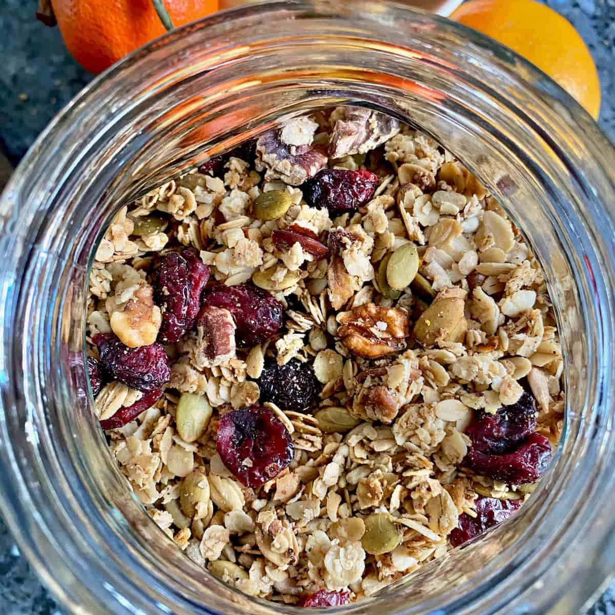 closeup of a glass cookie jar filled with toasted oats, nuts, seeds and dried cranberry fruits