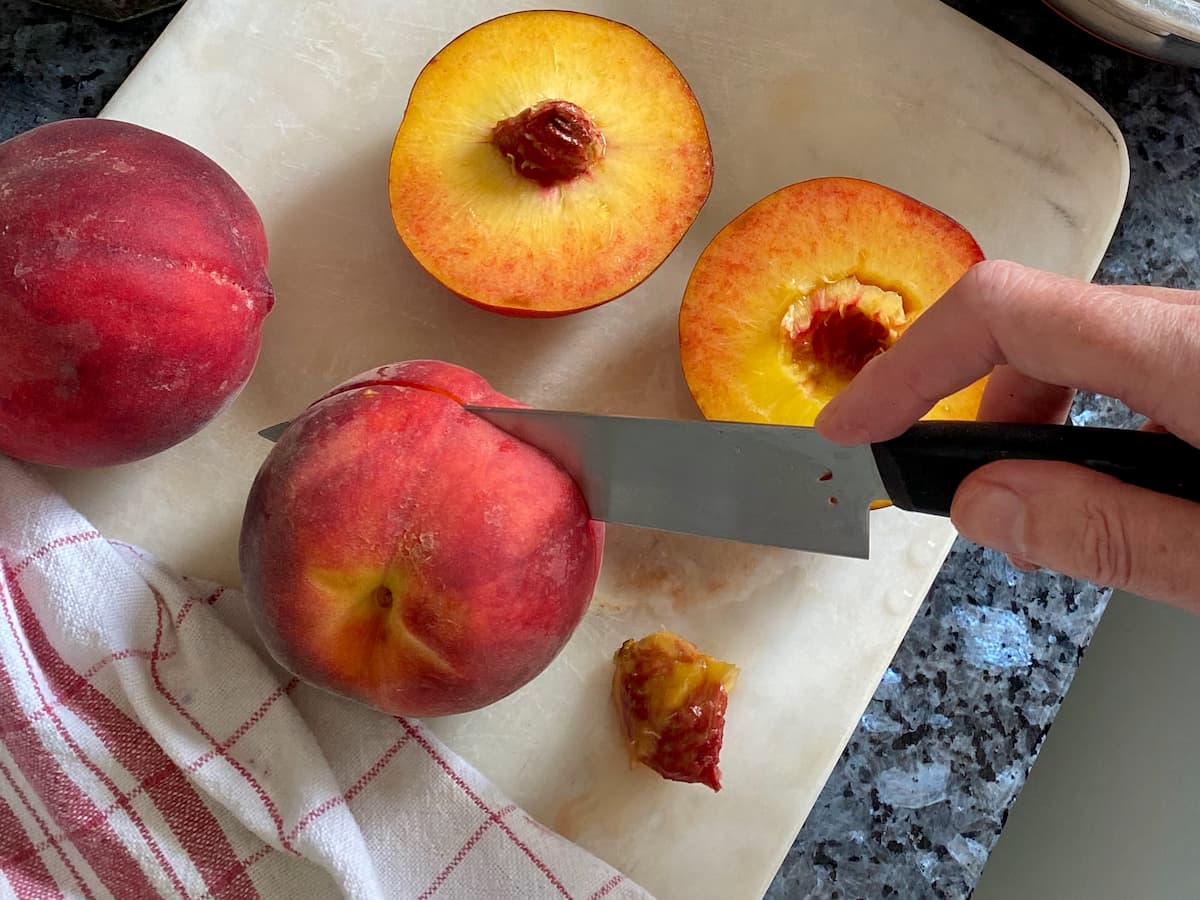 cutting half way through a peach with a sharp knife, horizontally under the peach's top