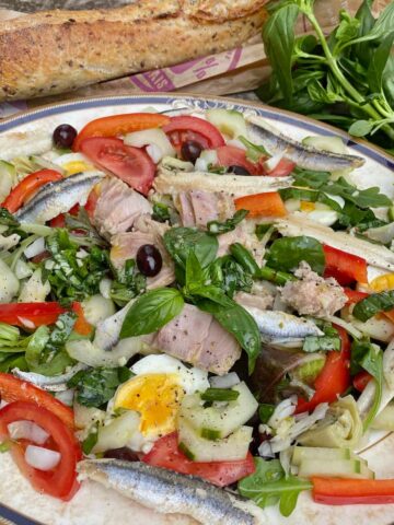 plate composed of a classic French salad Nicoise with many ingredients next to a basil plant and French baguette