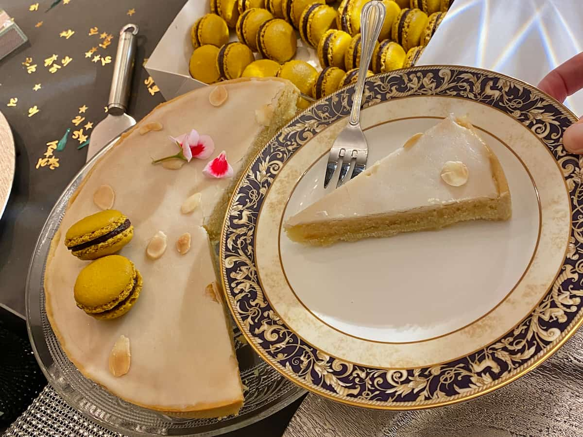 serving a slice of glazed almond cake topped with almonds and French macarons