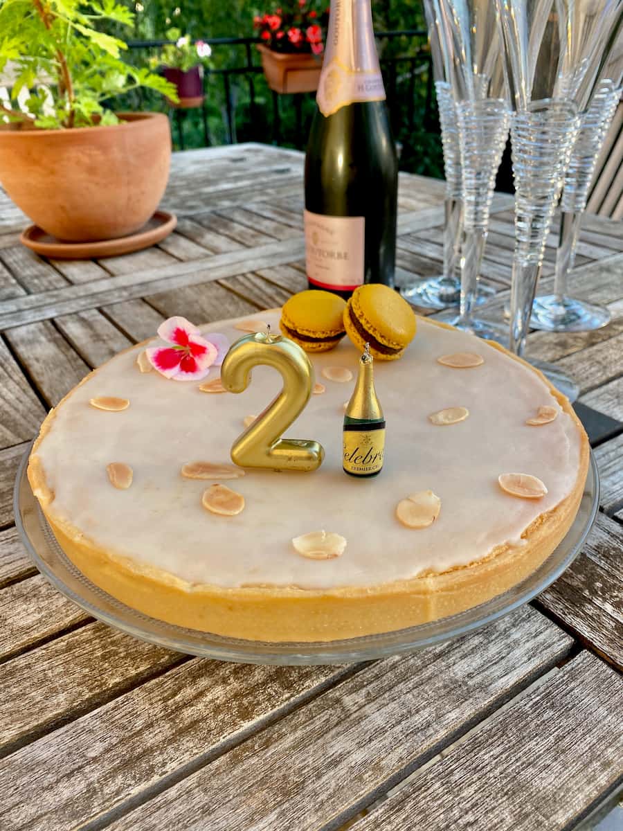 large glazed tart with toasted slivered almonds, macarons and 21st birthday candles next to Champagne