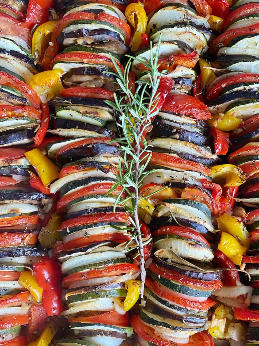 stacked roasted summer vegetables in a French tian dish with herbs and bay leaves
