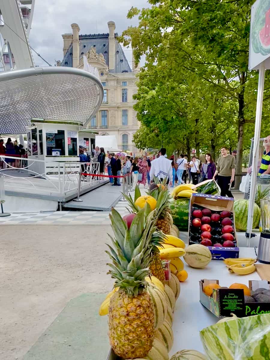 line up of pineapples and more fresh summer fruits at a stand in front of the giant Parisian wheel next to the Louvre