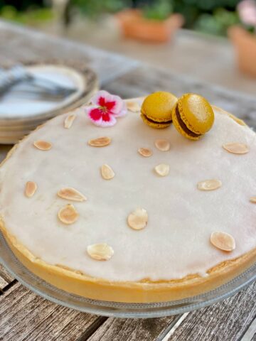 glazed round almond tart topped with toasted slivered almonds, a flower and French macarons