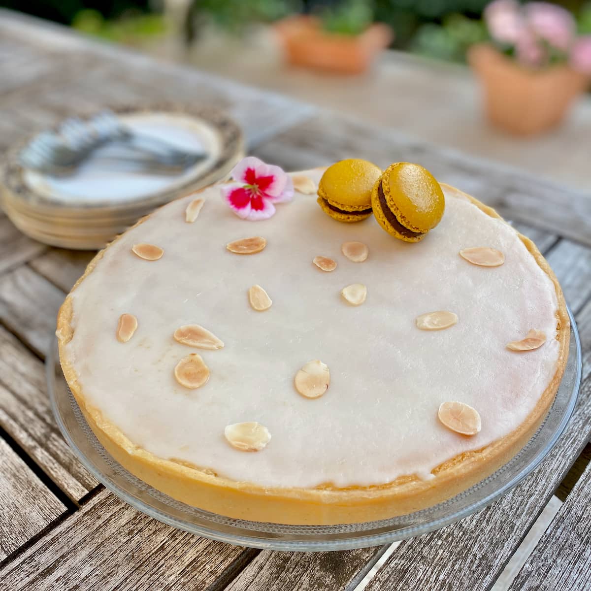 glazed round almond tart topped with toasted slivered almonds, a flower and French macarons
