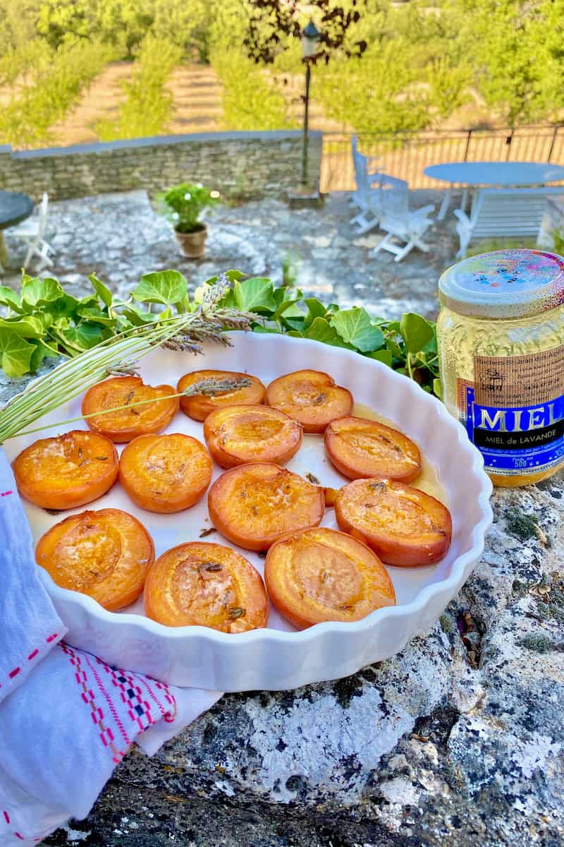 stonewear dish on a French wall in Provence with halved baked apricots, honey and lavender flowers