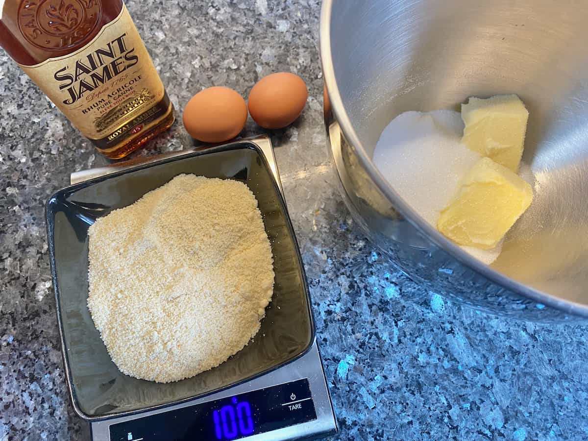 weighing out almond flour next to other ingredients such as dark rum, butter, sugar and eggs