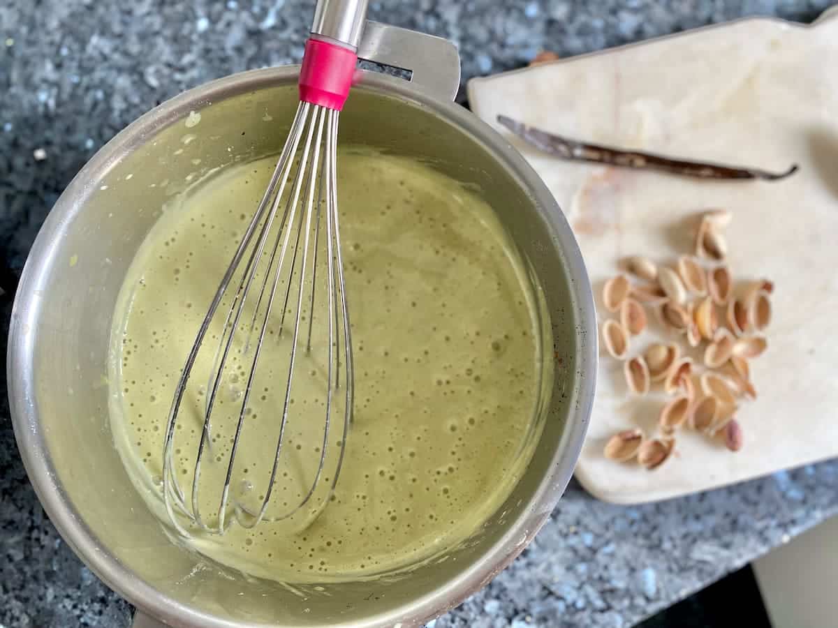 whisking pistachio custard in pan on counter to cool