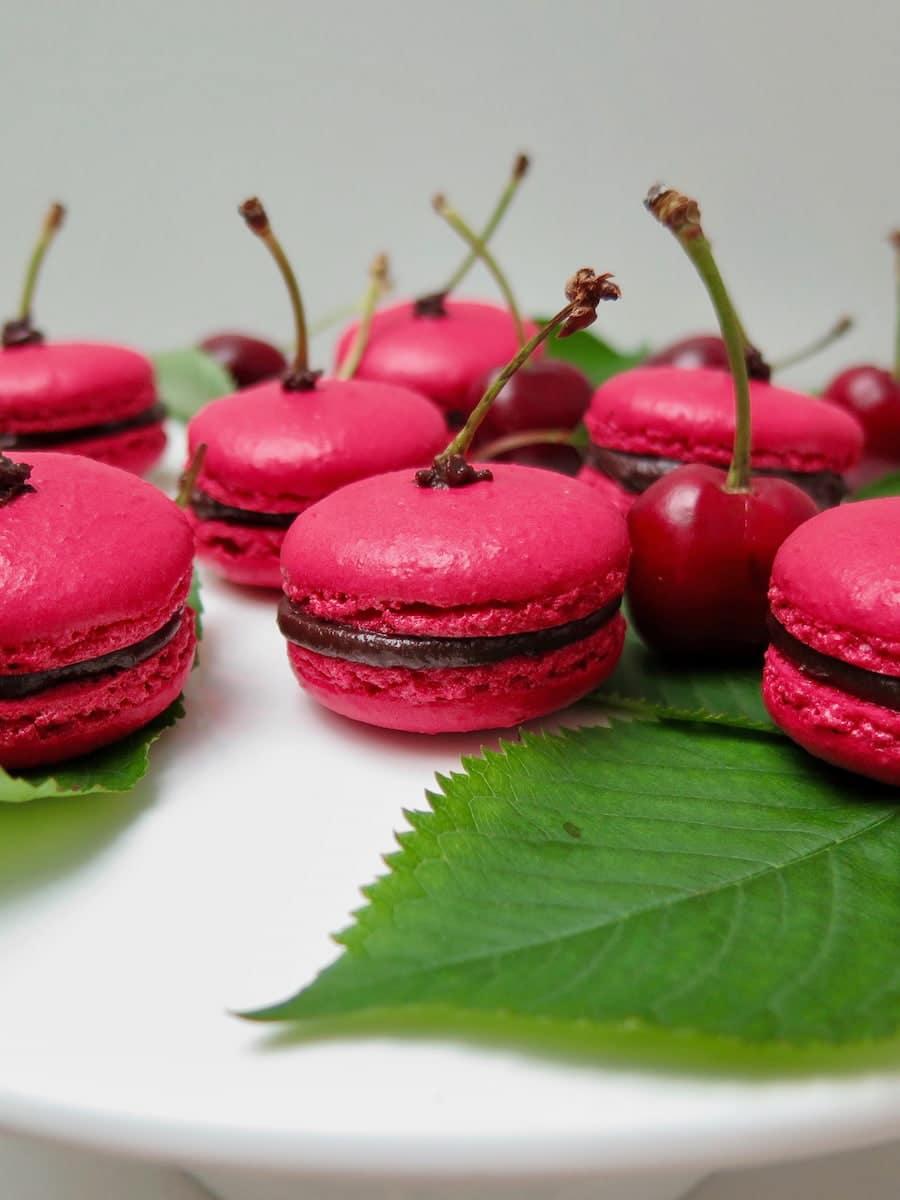 cherry pink macarons filled with lush chocolate ganache and decorated with cherry stalks