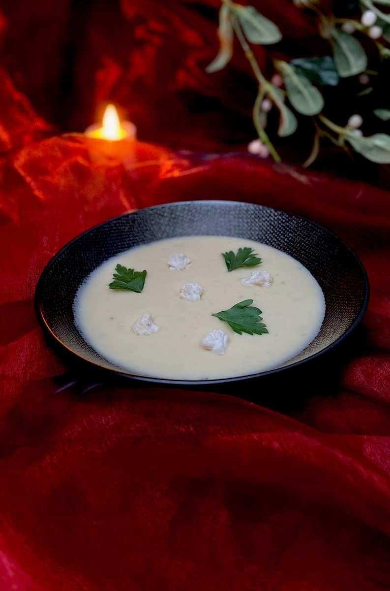 bowl of creamy cauliflower soup topped with a classic French garnish of raw florets and herbs