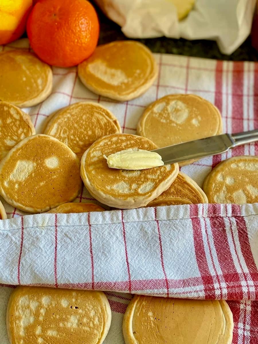 thick little round pancakes stacked together in a tea towel, spreading butter on one of them