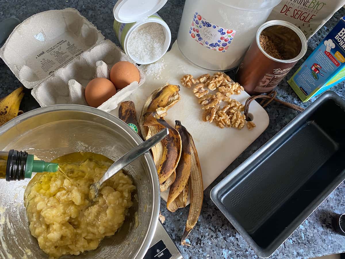 pouring oil into mashed bananas amongst ingredients for a banana coffee cake