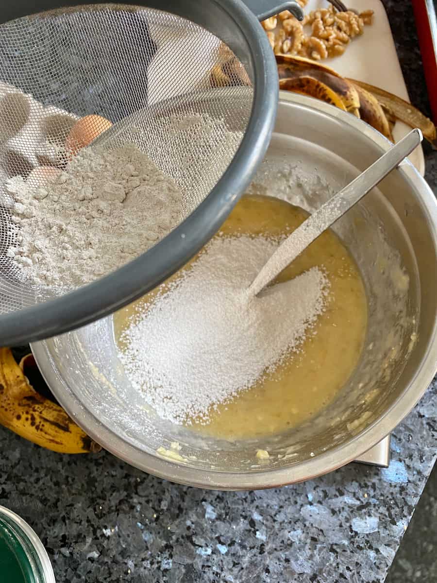 sifting flour into a bowl of mashed bananas and eggs