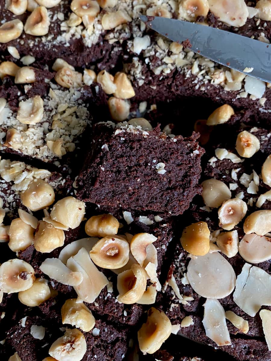 close up of a fudgy gluten free brownie square amongst toasted broken hazelnuts