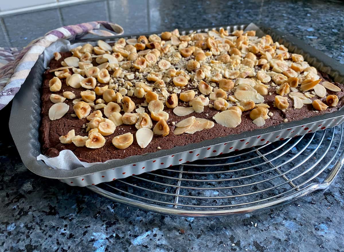 tray of gluten free brownies topped with toasted almonds and hazelnuts just out of the oven