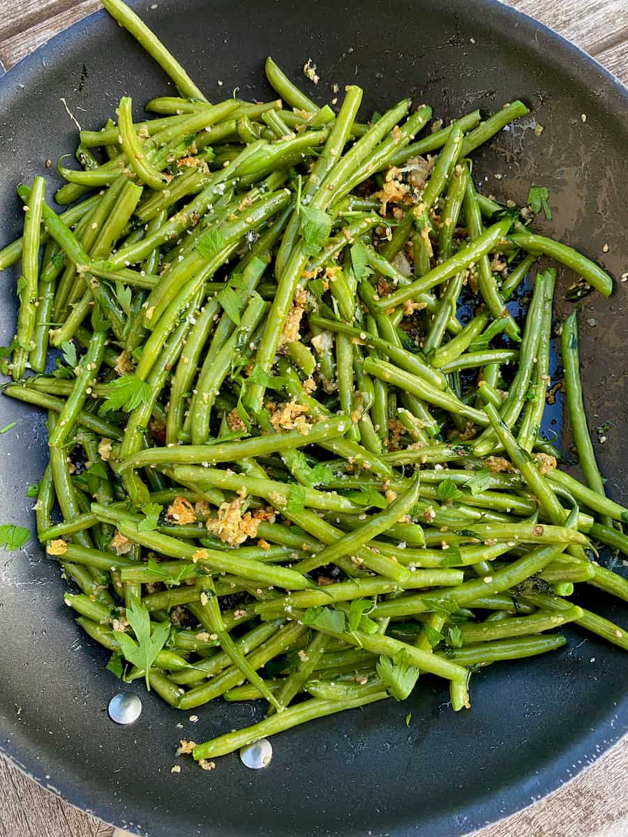 sautéed green beans in a pan with garlic, breadcrumbs, herbs and seeds