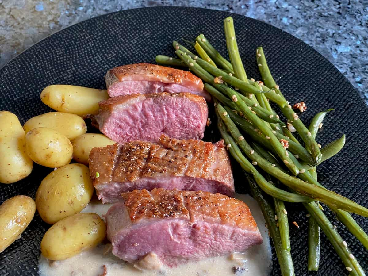 slices of seared pink duck breast with new potatoes and green beans sautéed in garlic and sesame seeds