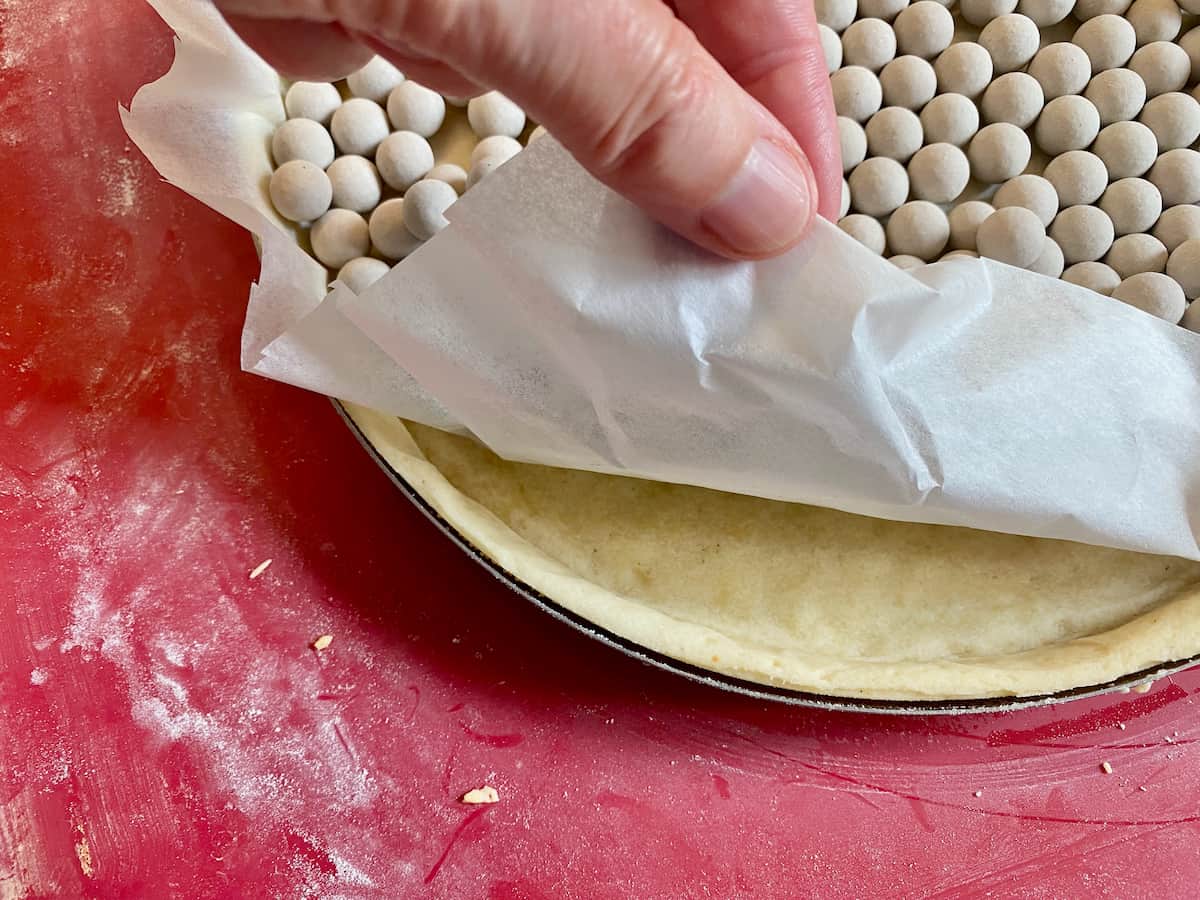 lifting baking paper with baking beans to reveal a perfectly cooked sweet tart shell