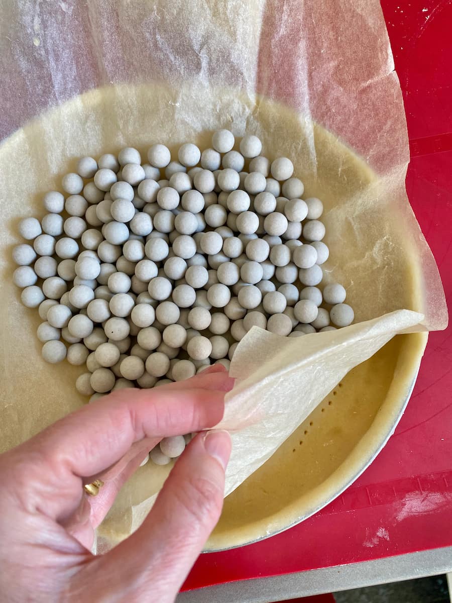 sneaking a peak under the baking paper and beans to reveal fork prickings in the tart dough