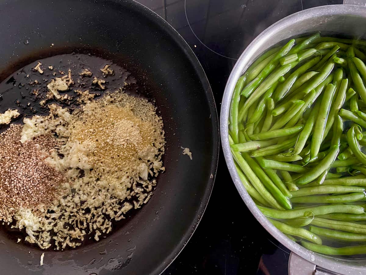frying pan with minced garlic, breadcrumbs, seeds in oil and butter next to a pan of cooking green vegetables