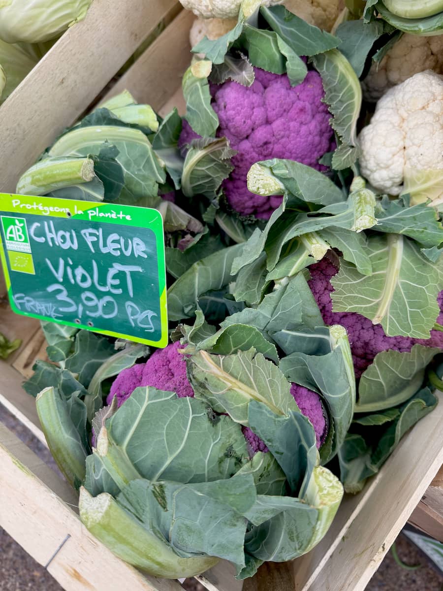 crate of French cauliflowers, including purple hidden in their leaves