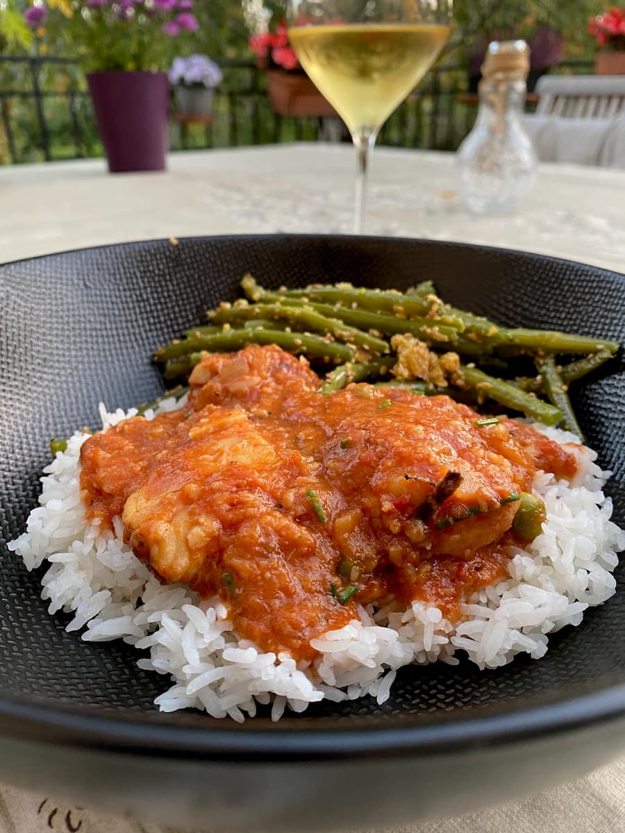 plate of fish stew with tomatoes on a bed of rice and green beans on the side