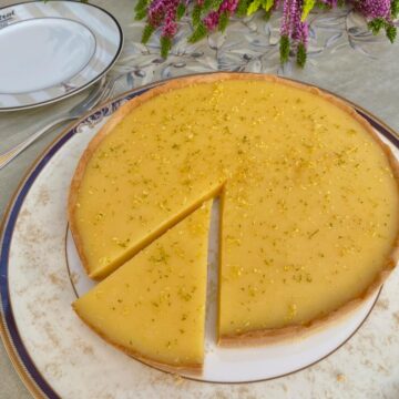 Lemon tart with slice cut out of it and topped with finely grated lemon and lime zest