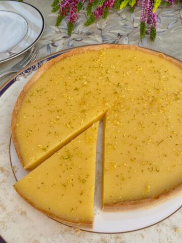 Lemon tart with slice cut out of it and topped with finely grated lemon and lime zest