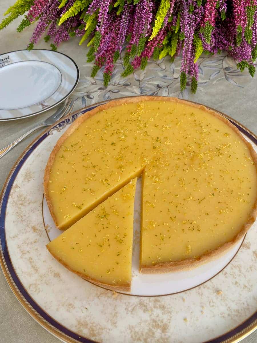 bright yellow lemon tart with a clean cut slice, topped with zest