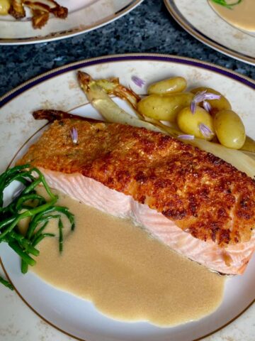 plates of herb crusted salmon with potatoes, asparagus and a butter sauce