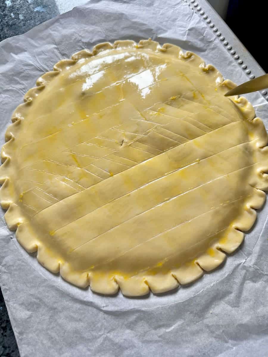decorating a puff pastry cake with a knife over chilled egg yolk glaze