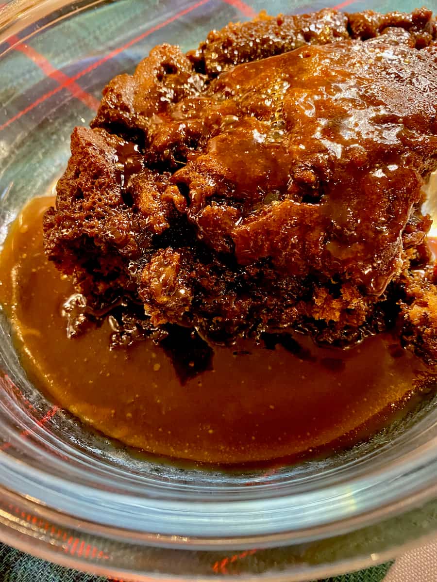 large extra moist sticky date pudding sitting in dark toffee sauce