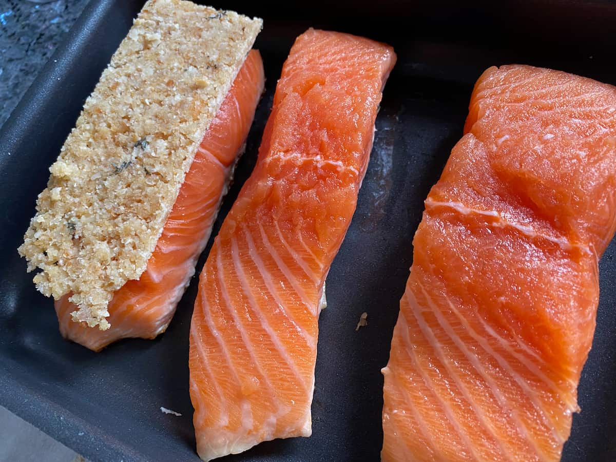 seared salmon fillets in a baking dish, one with a raw rectangular breadcrumb topping