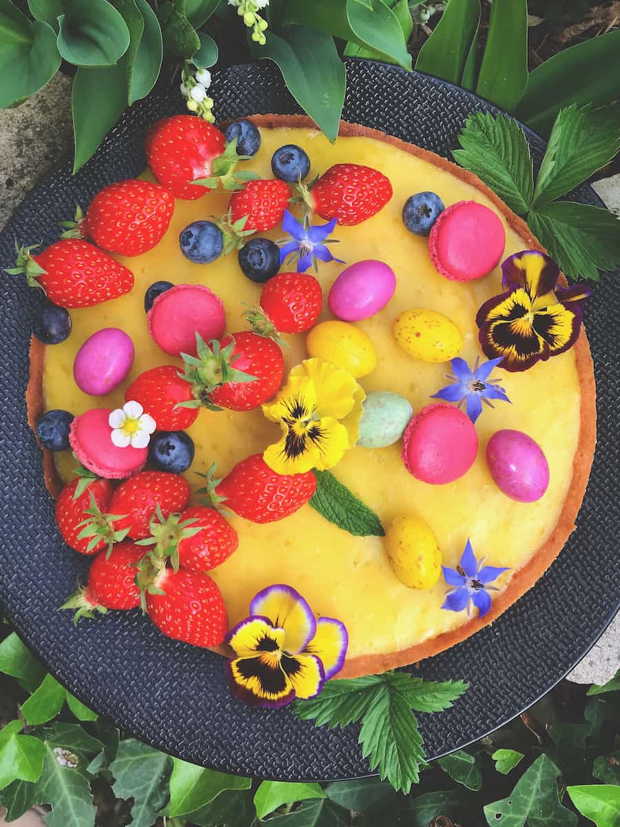 lemon tart decorated with strawberries, flowers and macaron shells