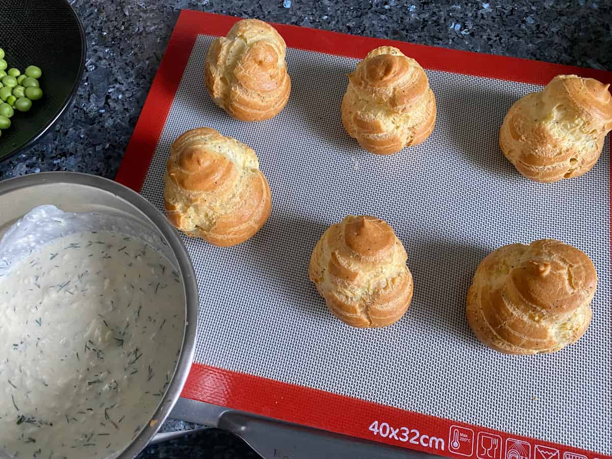 6 freshly baked choux buns out of the oven next to prepared apple, dill and cream sauce