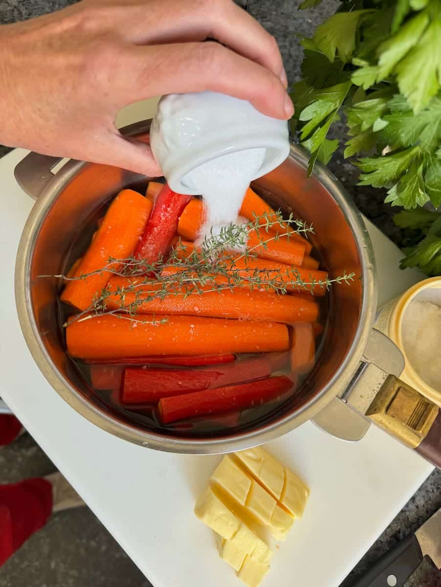 adding some sugar to prepared whole carrots in a pan of water