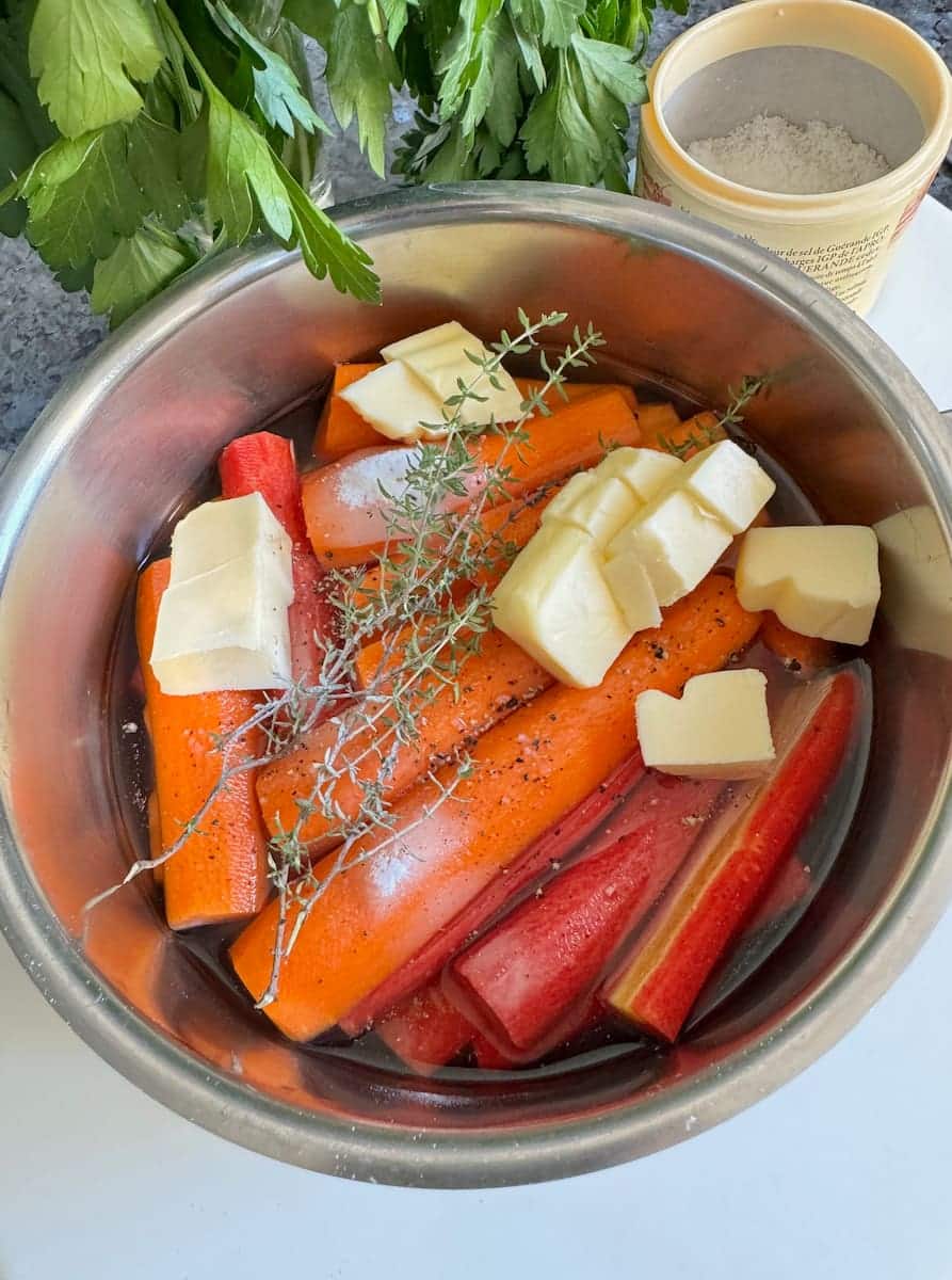 pan of raw chopped carrots topped with thyme, butter, water, sugar and salt