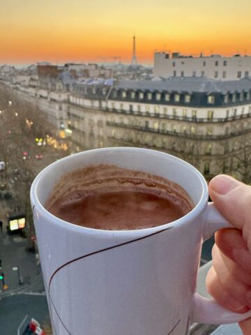 mug of French hot chocolate in front of a Paris skyline at sunset